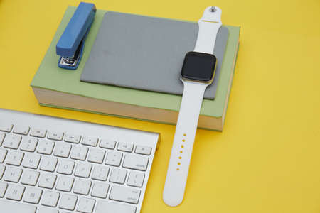 Digital learning concept . Top view of book, school supplier , wireless keyboard and smartwatch isolated on yellowの写真素材