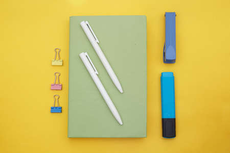 Top view of green book , white pen and school suppliers on yellow backgroundの写真素材