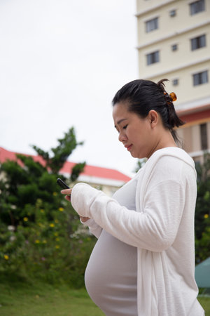 Asian Pregnant Woman in the park using smartphoneの写真素材