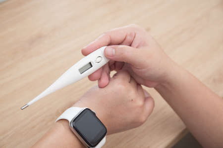 Closeup of woman looking at thermometer, hand holding a digital thermometer when measures the temperatureの写真素材