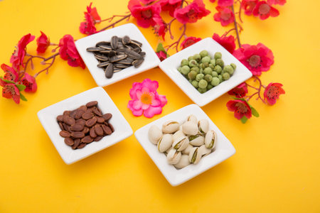 Pistachio nuts, seeds and flowers on yellow background.