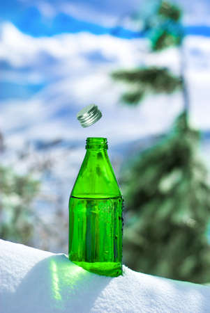Open glass bottle of mineral water on the backdrop of Alpine sceneryの写真素材