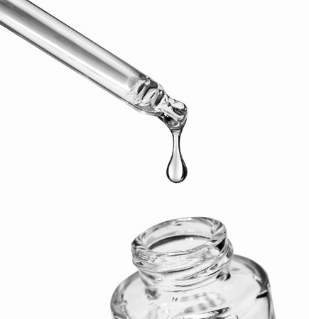 Drop falls from a pipette into a cosmetic bottle on white backgroundの写真素材