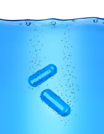 Two medical capsules dissolves in blue waterの写真素材