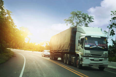 The truck drives on the highway winding through the landscape of the sunset forest.の写真素材