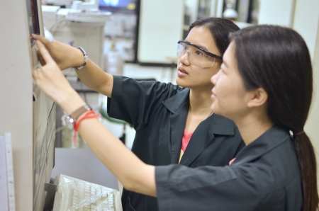 Female researcher teaching student about an apparatus in a laboratory.のeditorial素材