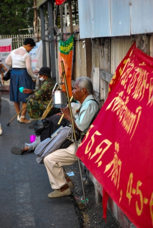 Thai blind man sits by the roadside and plays music for passing tourists and Thai people to make money.のeditorial素材