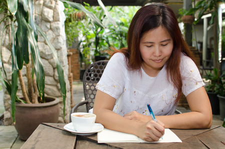 A happy Asian woman writing in backyard gardenの写真素材