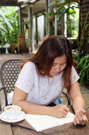 A happy Asian woman writing in backyard gardenの写真素材