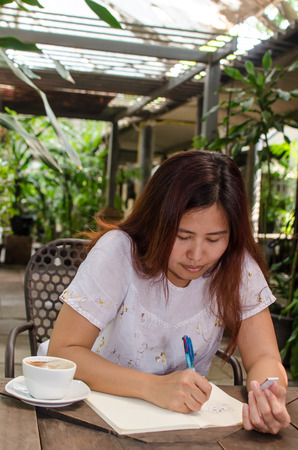 A happy Asian woman writing in backyard gardenの写真素材