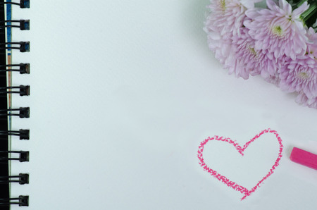 A white sketchbook and pink flower on black clothの写真素材