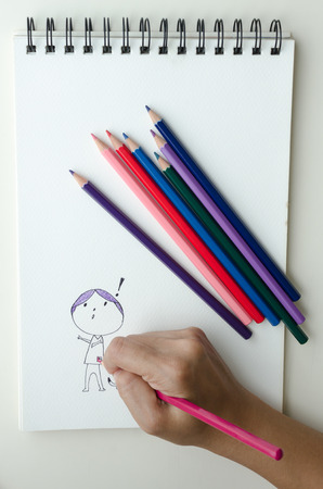Man sketching in a sketch book with colored pencils drawing an imaginative cartoon figure with an exclamation mark in a conceptual drawing, close up view from aboveの写真素材