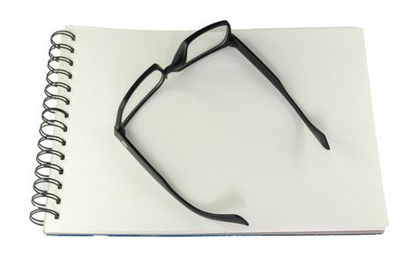 Pair of black framed glasses lying open on a spiral bound blank white sketch book, high angle view isolated on whiteの写真素材