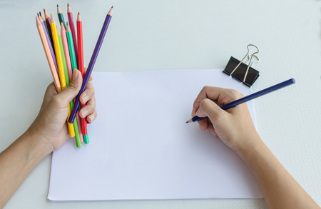 Man holding a fistful of colored pencils in one hand while commencing sketching in a sketch book to show off his creativity and artistic skills with the other, view from aboveの写真素材