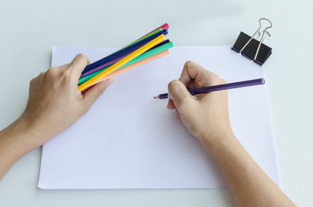 Man holding a fistful of colored pencils in one hand while commencing sketching in a sketch book to show off his creativity and artistic skills with the other, view from aboveの写真素材