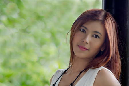 Beautiful happy young Asian woman in a park  with a delightful smile as she stands enjoying a hot summer dayの写真素材