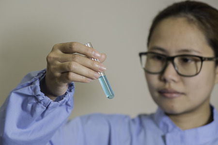Young female Asian lab worker wearing spectacles reading a chemical test checking the color of the solution in a test tubeの写真素材