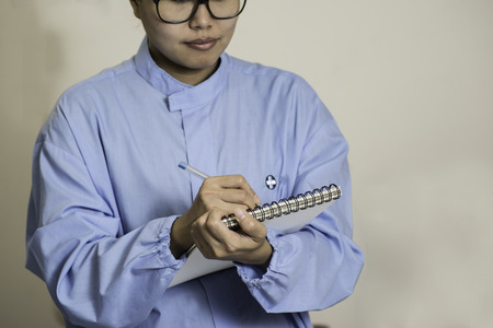 Young female Asian lab worker wearing spectacles writing on the lab notebookの写真素材