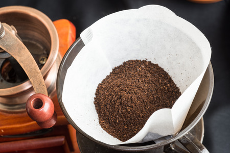 View from above of freshly ground coffee beans in a clean filter paper with a mill or grinder alongside conceptual of preparing a fresh cup of coffeeの写真素材