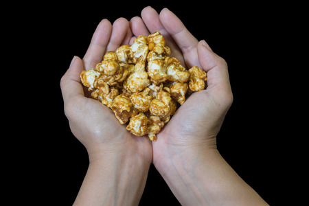 Cupped hands holding a handful of freshly caramel  popcorn isolated over blackの写真素材