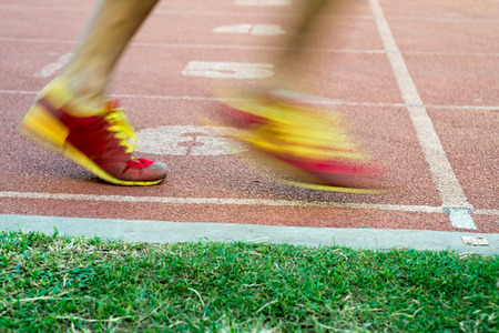 Side low angle view of unidentifiable runners leaving a racing track starting line in fast motionの写真素材