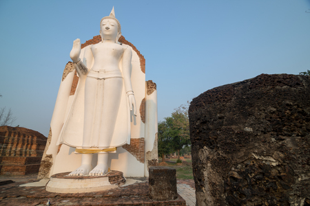 White Buddha statue in ruins temple facing morning sunlight and clear blue skyの写真素材