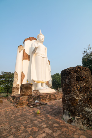 White Buddha statue in ruins temple facing morning sunlight and clear blue skyの写真素材