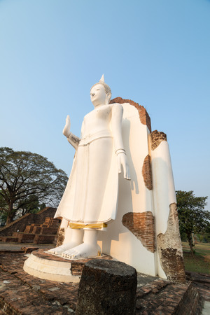 White Buddha statue in ruins temple facing morning sunlight and clear blue skyの写真素材