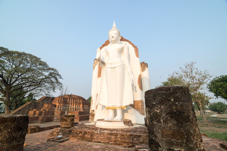 White Buddha statue in ruins temple facing morning sunlight and clear blue skyの写真素材