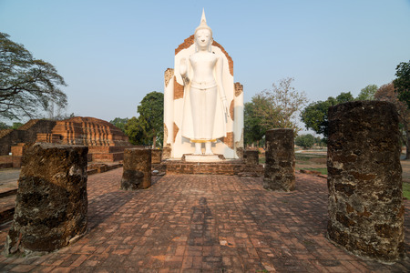 White Buddha statue in ruins temple facing morning sunlight and clear blue skyの写真素材