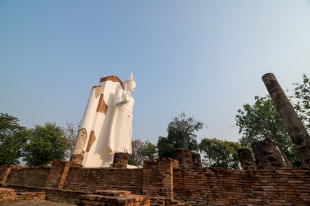 White Buddha statue in ruins temple facing morning sunlight and clear blue skyの写真素材