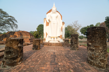 White Buddha statue in ruins temple facing morning sunlight and clear blue skyの写真素材