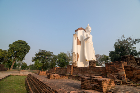 White Buddha statue in ruins temple facing morning sunlight and clear blue skyの写真素材