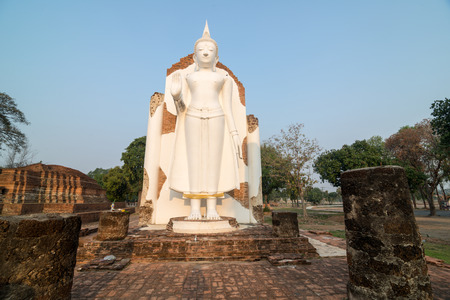 White Buddha statue in ruins temple facing morning sunlight and clear blue skyの写真素材