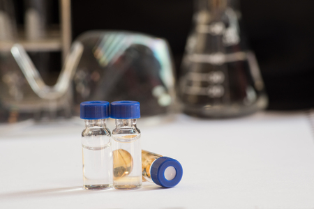 Blue cap vials and out of focus laboratory glassware containing chemicals in science researchの写真素材