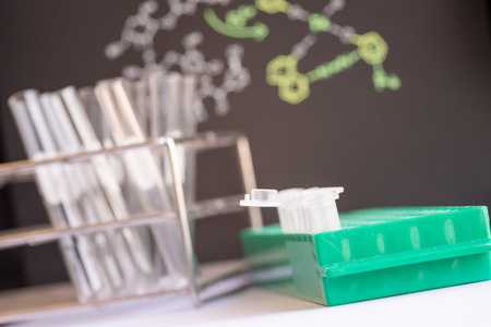 Plastic vials places in green rack in front of chemical formula and test tubeの写真素材