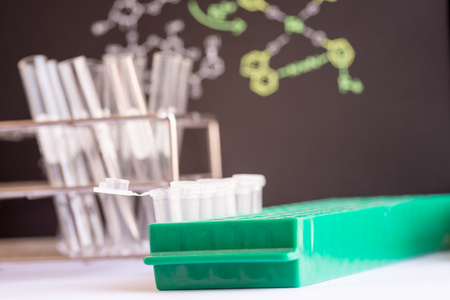 Plastic vials places in green rack in front of chemical formula and test tubeの写真素材