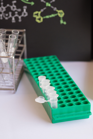 Plastic vials places in green rack in front of chemical formula and test tubeの写真素材
