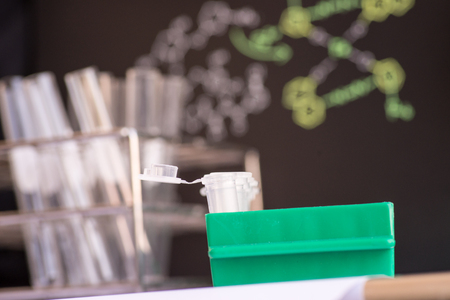 Plastic vials places in green rack in front of chemical formula and test tubeの写真素材