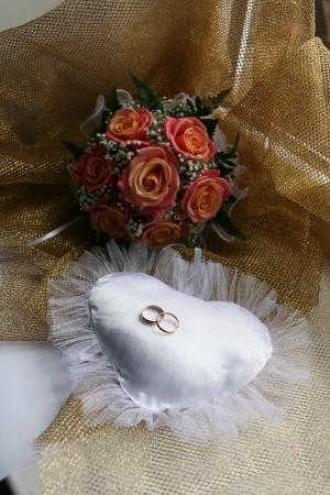 Wedding rings on white pillow in the form of the heart near the wedding bouquetの写真素材