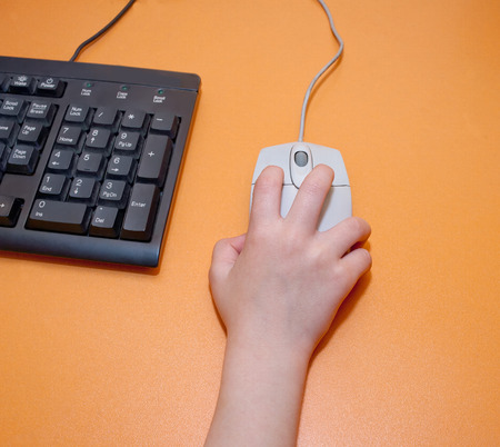 Children's right hand on a gray computer mouse on orange tableの写真素材
