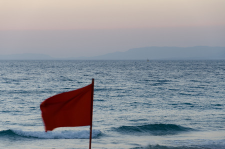 Red flag at sand beach with sea and visible islandの写真素材