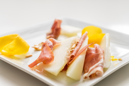 Prosciutto slices with yellow lemon on white plate wih seeds and peel. Very soft focus.の写真素材
