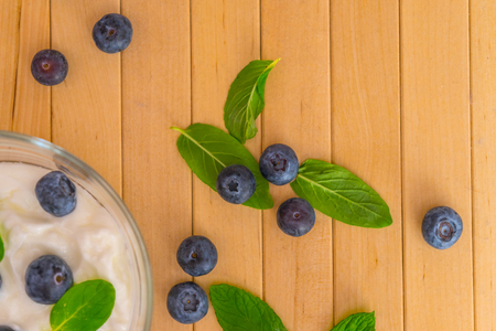 Blueberries with yogurt and mint leafs on wooden table. Blueberries with yogurt and mint in transparent bowl. Transparent bowl with yogurt, blueberries and mint. Soft focus. Top or flat view.の写真素材