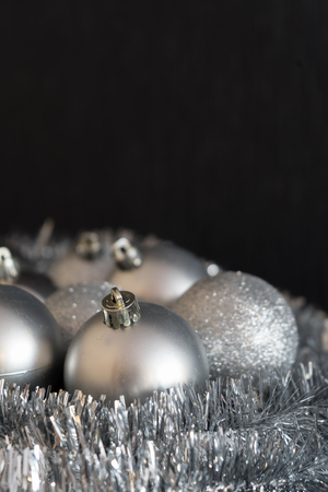 Vertical photo of shiny and bright silver christmas balls decoration lying on silver christmas chain on dark black structured background in very soft focus.の写真素材