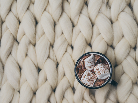 Cozy composition, hot chocolate with marshmallows, merino wool blanket, warm and comfortable atmosphere. Knit background. Flat lay. Top view. Copy space. Autumn concept.