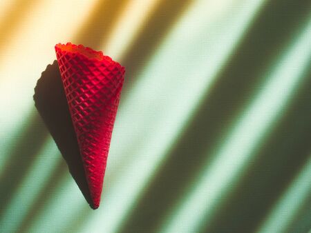 Red ice cream cone on light blue background with shadows.の写真素材