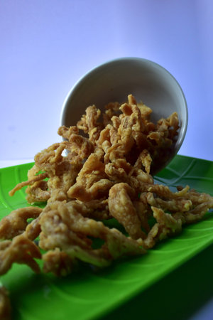 Oyster mushroom chips, crispy, savory spilling out of a white bowl on a green plate
