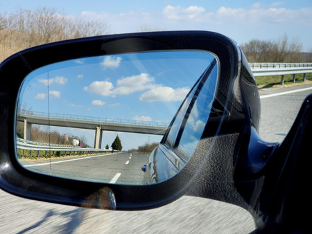 Landscape and road reflection in car rearview black mirror.