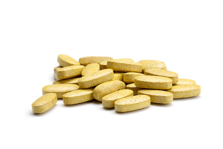 Close-up of a pile of yellow and brown colored pills or capsules on isolated white background....